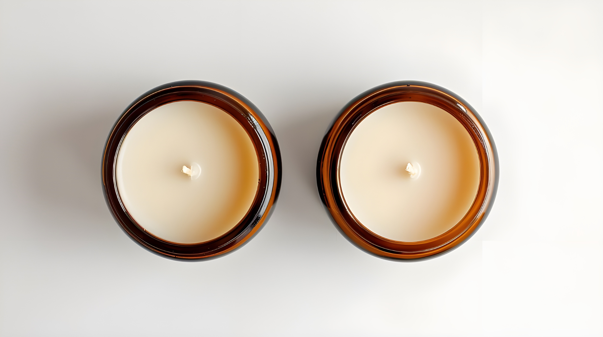 Two amber glass candles viewed from above on a clean light background.